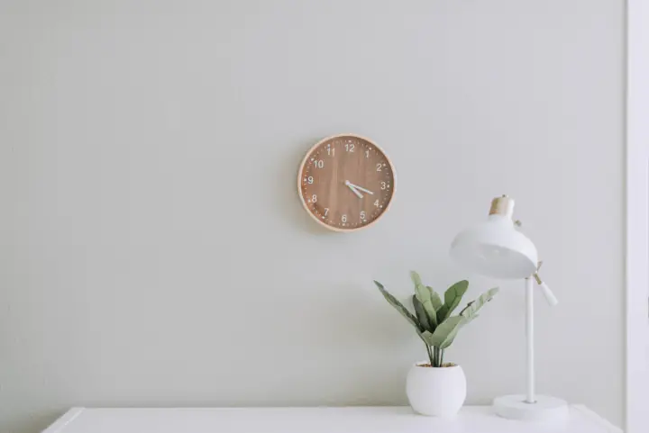 Glatte, hell gestrichene Wand mit Uhr, Pflanze und Lampe