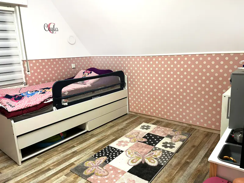 Kinderzimmer mit rosa gepunkteter Tapete unter der Dachschräge