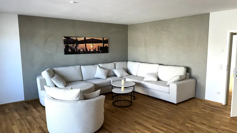 Wohnzimmer mit weißer Sofaecke vor einer Wand in grauer Betonoptik
