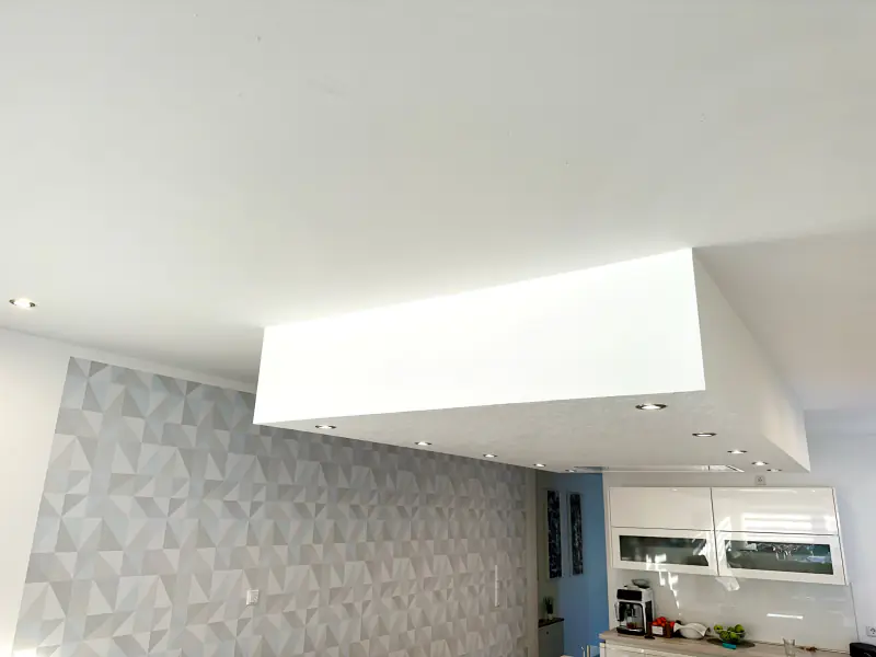 Abgehängte Decke mit Einbaustrahlern über einer Küche, daneben eine Wand mit Mustertapete