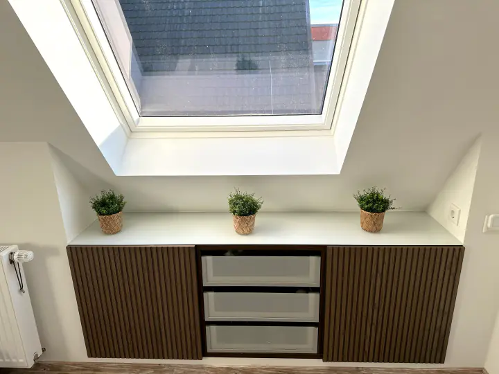 Verkleidete Dachschräge mit Dachfenster über einem Sideboard mit Holzfronten